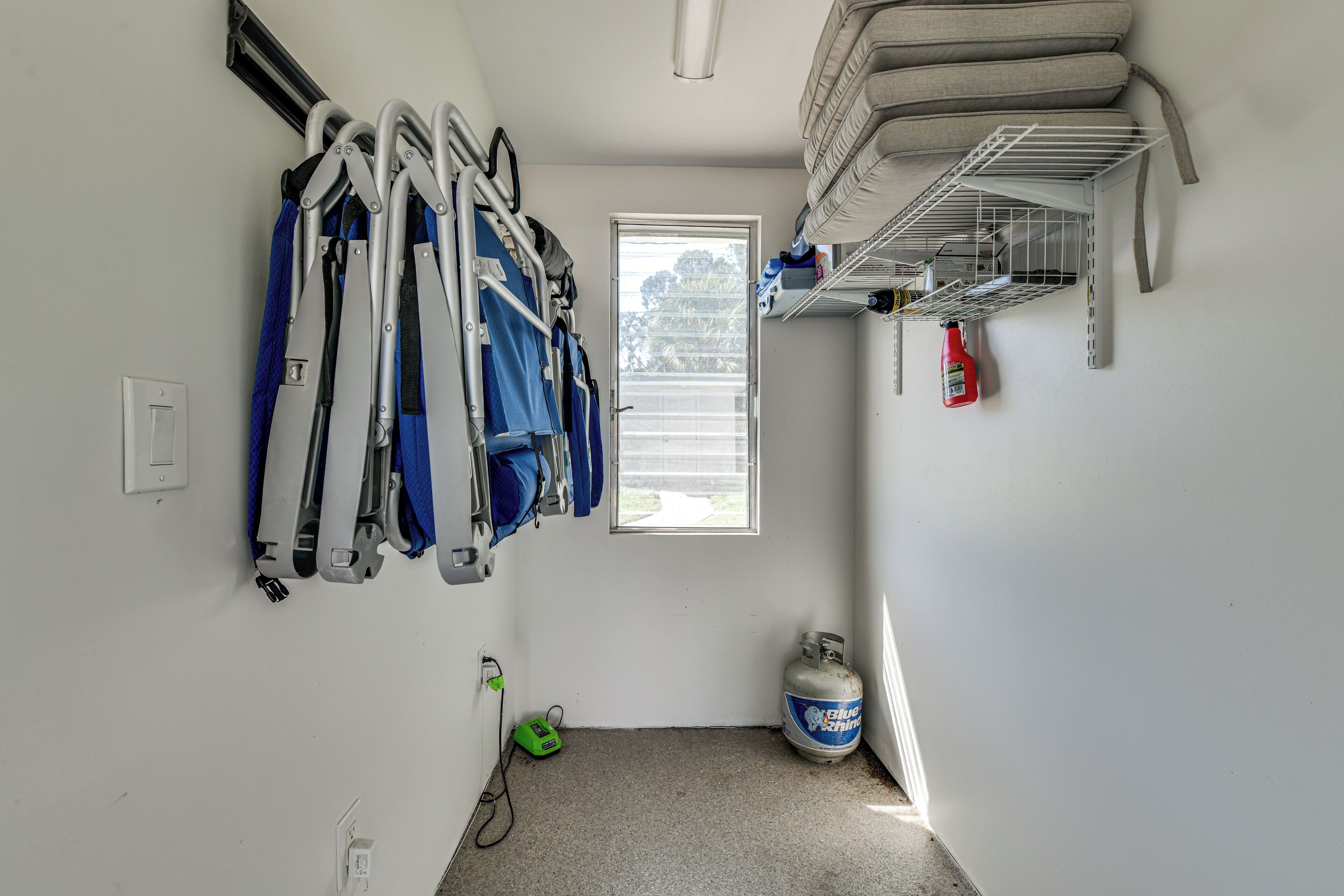 A room with a window, a gas cylinder, a shelf with cleaning supplies, and a wall-mounted rack with crutches.
