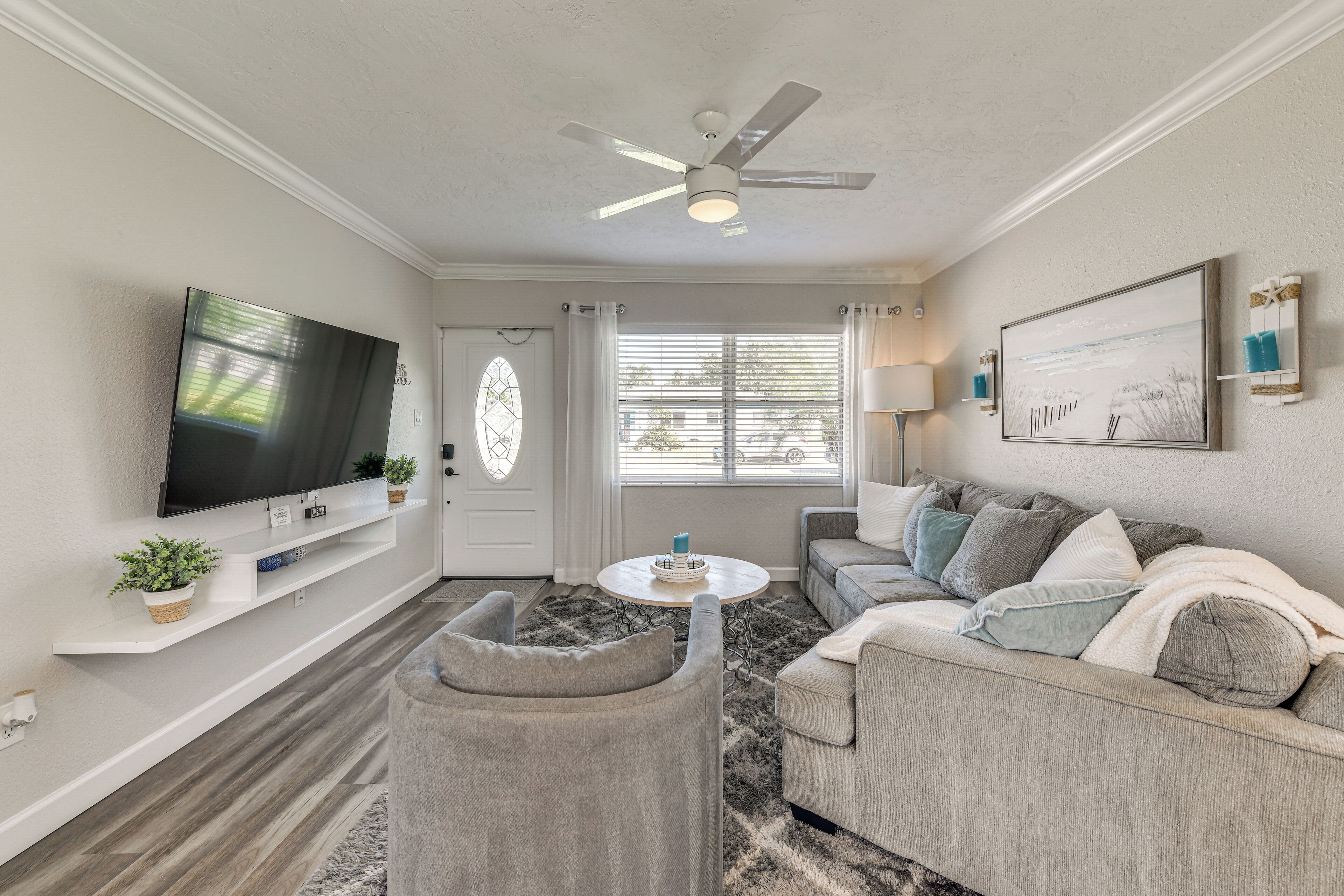 A living room with a flat-screen TV, ceiling fan, sofa, and a small table with a candle.