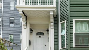 Un porche con una puerta blanca marcada '60', una pequeña escalera y revestimiento verde en la casa.