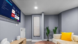 Una sala de estar moderna con una televisión de pantalla plana, una mesa de centro de madera, un sofá con un cojín amarillo y una planta.