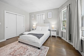 A bedroom with a bed, bedside tables, a nightstand, a rug, and a window with curtains. - Spacious Fort Hill 3BR | Sleeps 10 (Boston)