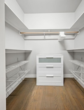 A walk-in closet with white shelving units, a wooden rod, and a white chest of drawers. - Spacious Fort Hill 3BR | Sleeps 10 (Boston)