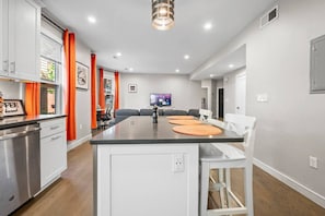 A modern kitchen with a central island, white cabinetry, and orange curtains. - Spacious Fort Hill 3BR | Sleeps 10 (Boston)