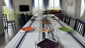 Un espace repas avec une longue table dressée pour le repas, un téléviseur accroché au mur et une vue sur l’extérieur.