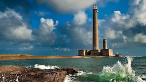 Un phare doté d’une haute tour, d’une base comportant de nombreuses fenêtres et d’une côte rocheuse où les vagues s’écrasent.