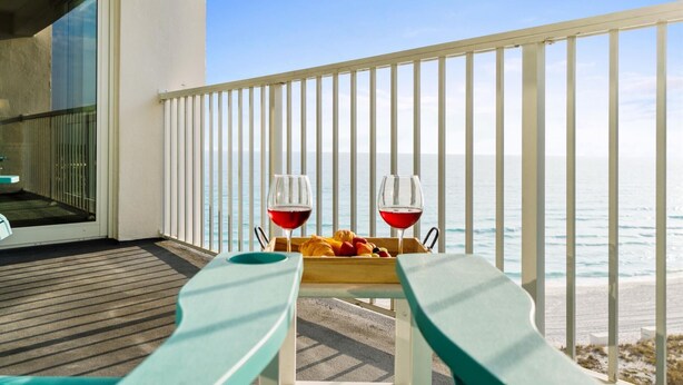 Un balcón con vista al mar, dos copas de vino tinto y una bandeja de fruta.