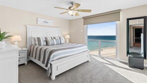 Un dormitorio con cama, lámparas de noche, ventilador de techo, vista a la playa y puerta al exterior.