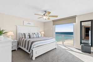 A bedroom with a bed, bedside lamps, a ceiling fan, a view of the beach, and a door to the outside. - Shoreline Towers 1094-seasonal beach service-pool (Destin)