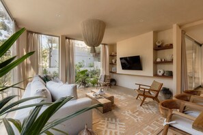 A modern living room with a sofa, coffee table, and chairs, a TV mounted on the wall, and a large window with curtains. - Villa Ka'an Pura Selva luxury and nature near the beach (Tulum)