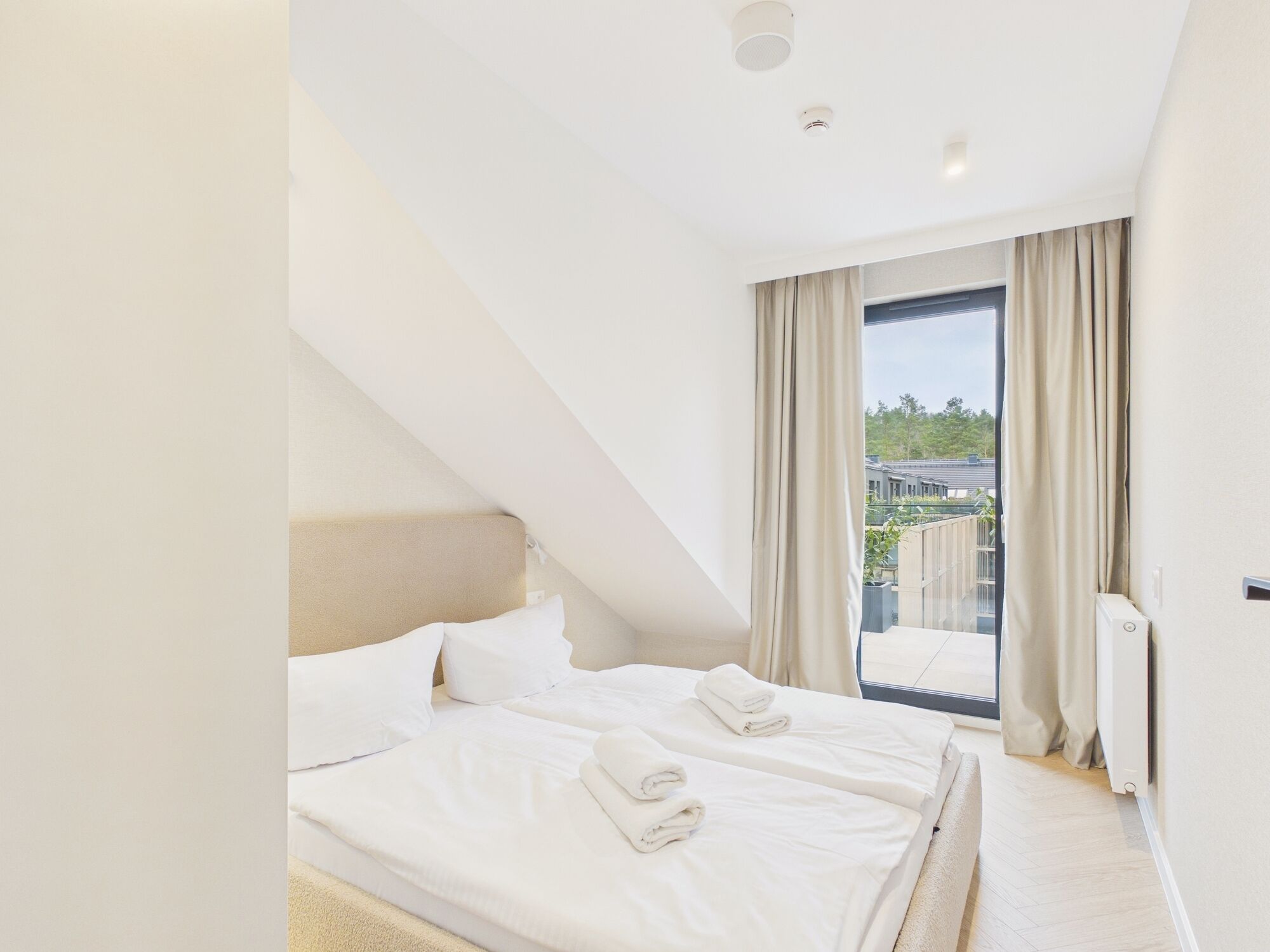 Een slaapkamer met twee bedden, een groot raam met gordijnen en uitzicht op de omgeving.