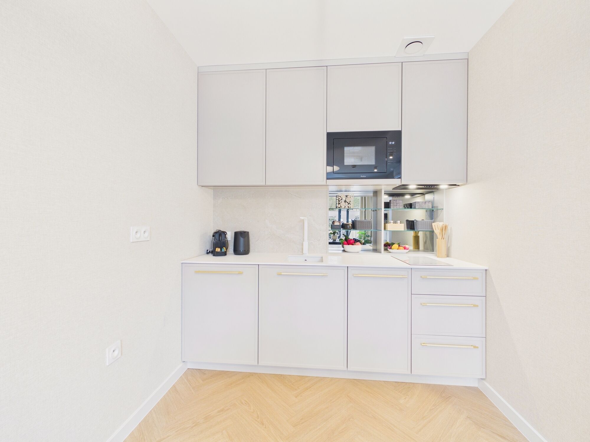 Una cocina moderna con armarios blancos, microondas, cafetera y frutero.