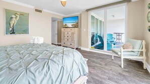 A bedroom with a bed, a ceiling fan, a painting, a dresser, and a view of the balcony. - Shoreline Towers 3023 -seasonal beach service pool-near beach (Destin)