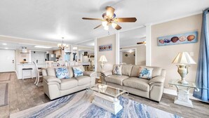 A spacious living room with a ceiling fan, a dining area, and a kitchen in the background. - Shoreline Towers 3023 -seasonal beach service pool-near beach (Destin)
