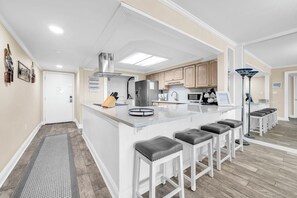 A modern kitchen with a central island, bar stools, and a built-in stove. - Shoreline Towers 3023 -seasonal beach service pool-near beach (Destin)