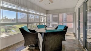 Eine überdachte Terrasse mit Korbmöbeln, einem Deckenventilator und großen Fenstern mit Blick ins Freie.