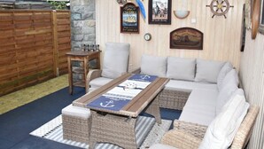 Un espacio exterior acogedor con una mesa de mimbre, sillas acolchadas y decoración náutica.