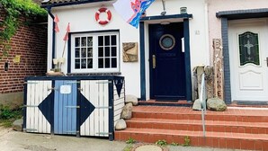 Una casa con puerta azul, pared blanca y una bandera.