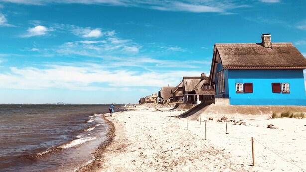 Una playa con casas de techo de paja y un cielo azul despejado.
