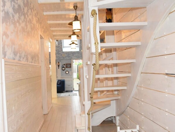 A spiral staircase with white railings and a rope handrail, leading to an upper floor.