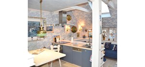 A compact kitchen with a dining area, a blue sofa, and a view of the sea.