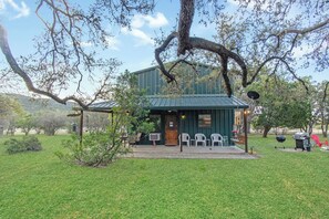 A rustic building with a green roof, surrounded by trees and grass. - Cherry Creek Cabin | Near Garner | Frio | Concan (Concan)