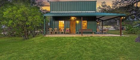 A two-story building with a covered porch, a wooden door, and a seating area with chairs and tables.