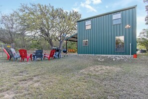 A green metal building with a covered outdoor seating area and several Adirondack chairs. - Cherry Creek Cabin | Near Garner | Frio | Concan (Concan)