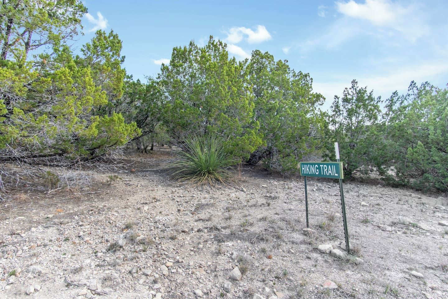 A hiking trail sign in a natural, rocky terrain with sparse vegetation.