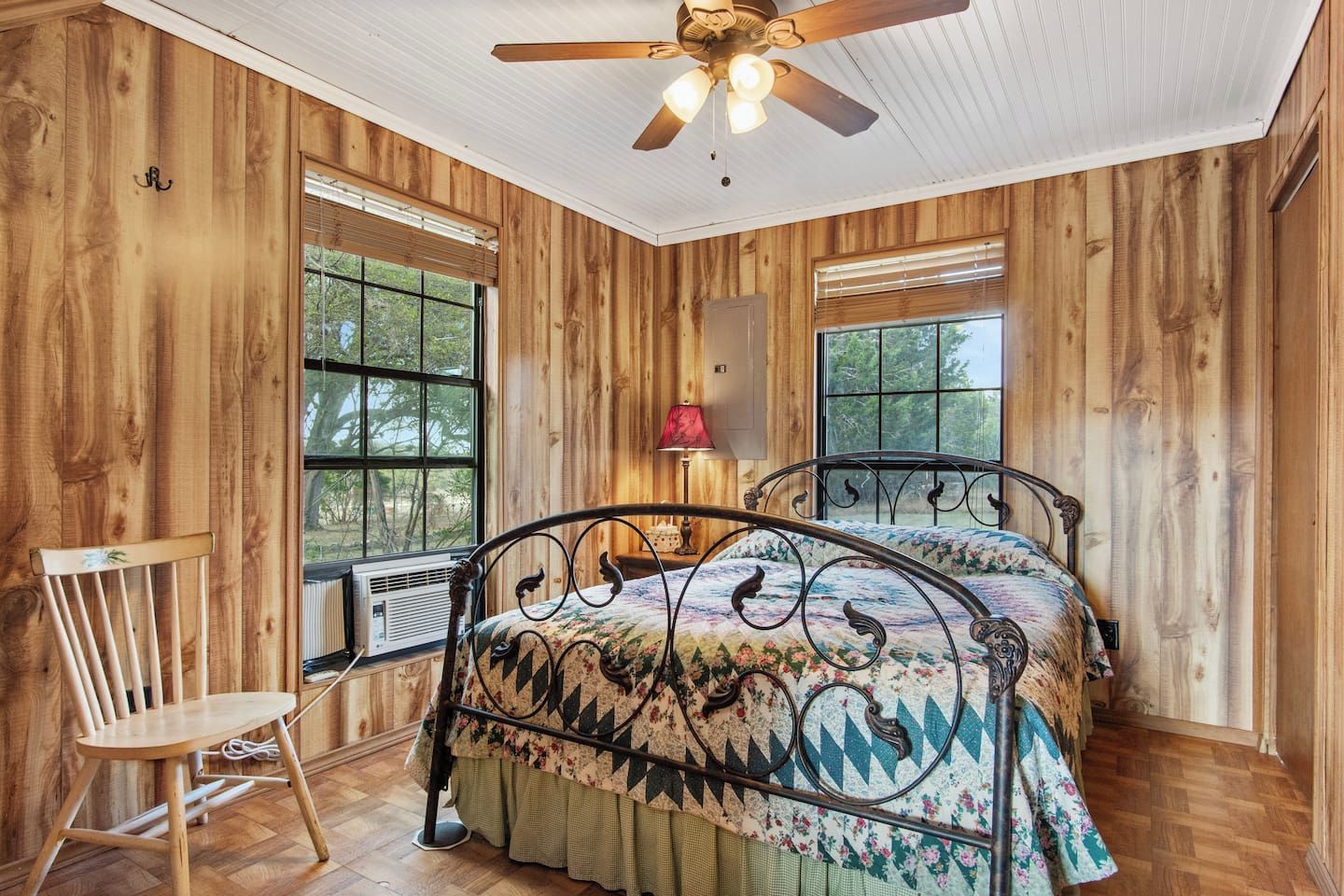 A wooden-paneled room with a bed, a chair, and a ceiling fan.