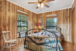 A wooden-paneled room with a bed, a chair, and a ceiling fan. - Cherry Creek Cabin | Near Garner | Frio | Concan (Concan)