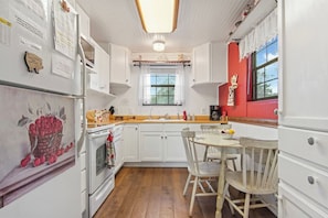 A compact kitchen with white cabinets, a wooden countertop, and a dining area with a table and chairs. - Cherry Creek Cabin | Near Garner | Frio | Concan (Concan)