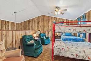 A bunk bed with a red frame, a single bed with a blue bedspread, two green armchairs, a wooden wall, a ceiling fan, and a wooden floor. - Cherry Creek Cabin | Near Garner | Frio | Concan (Concan)