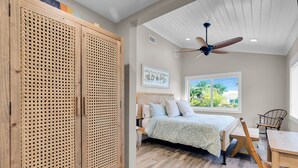 Ein Schlafzimmer mit einem Bett, einem Deckenventilator, einem Fenster mit Blick und einem Holzschrank.