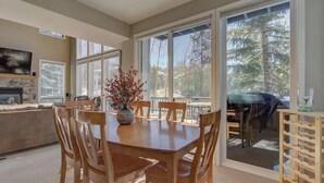 A dining area with a table, chairs, a vase with flowers, and a view of trees through large windows. - Walk To Skiing, Quiet Neighborhood, Big House (Steamboat Springs)