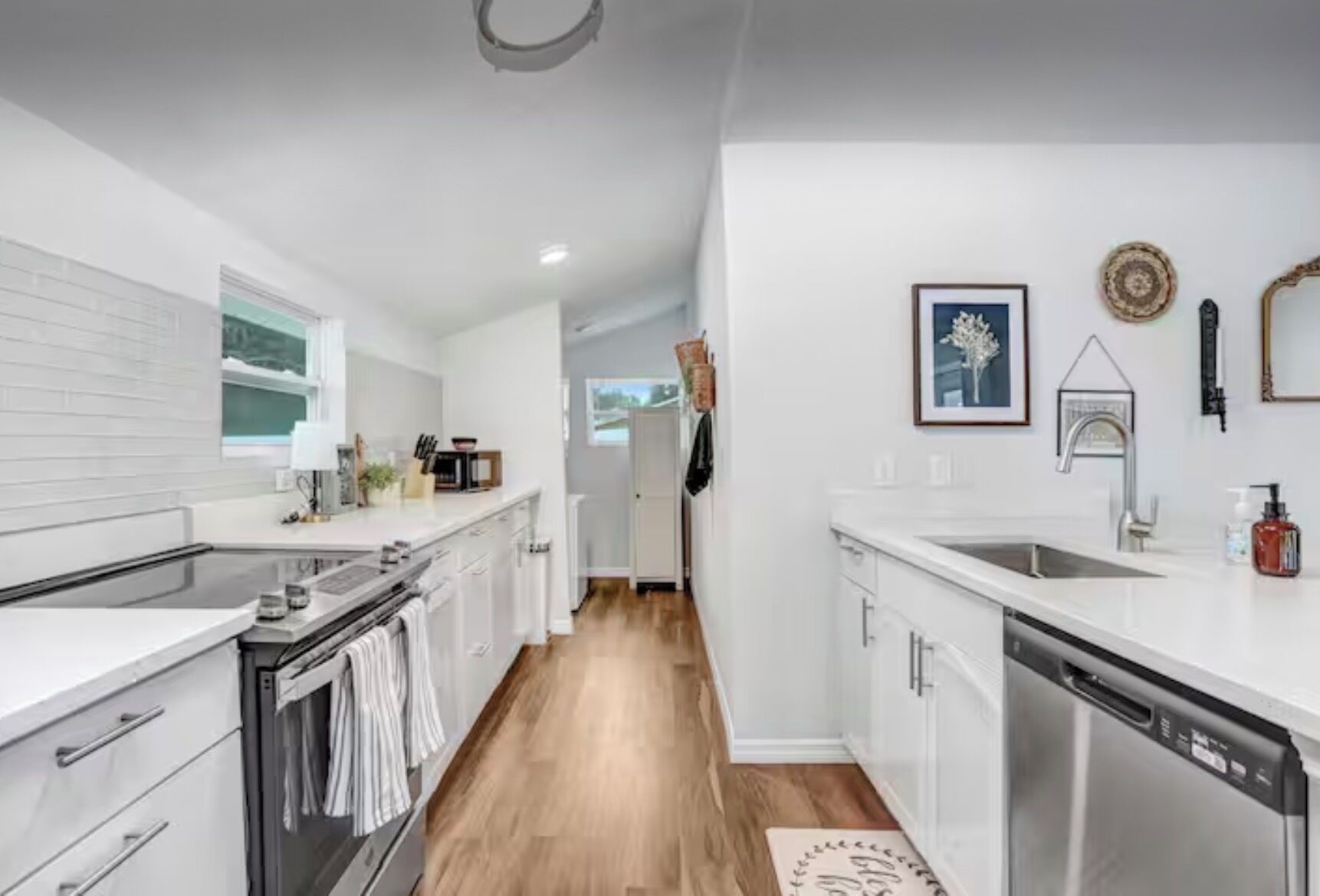 A modern kitchen with white cabinetry, stainless steel appliances, and a wooden floor.