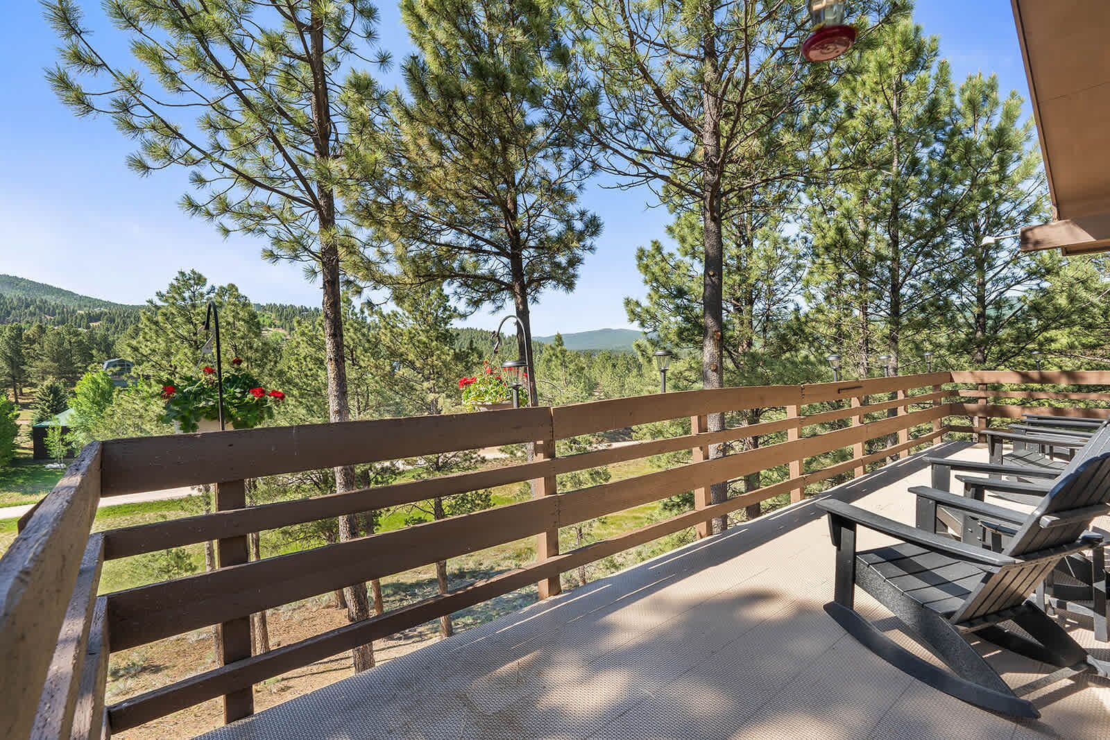 Una terraza de madera con bancos y mesas, rodeada de pinos y vistas al paisaje.