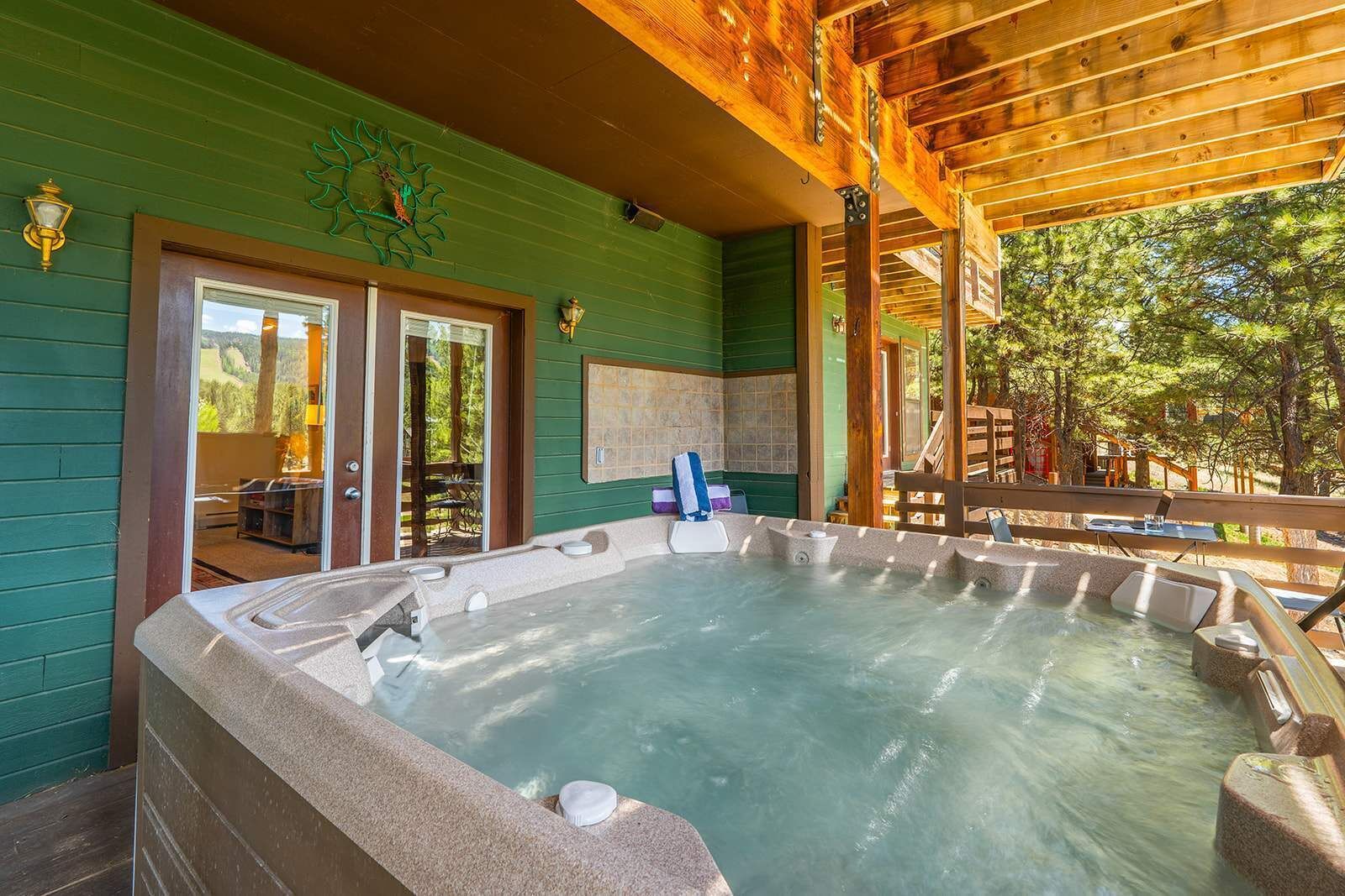 A hot tub in a covered outdoor area with wooden beams and a green wall.