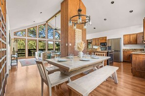 A modern kitchen with wooden cabinets, a large island, and a dining area with a bench. - Mountain-View Cabin | Hot Tub + Cozy Wood Stove (Angel Fire)