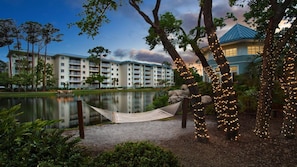 A hotel with multiple balconies, a lake, and string lights on trees.