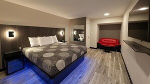 A modern hotel room with a large bed, a red sofa, a flat-screen TV, and a mirror. - Star Inn & Suites (Chicago Heights)
