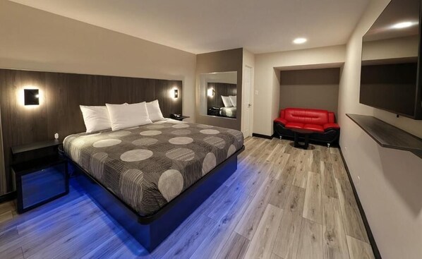 A modern hotel room with a large bed, a red sofa, a flat-screen TV, and a mirror.