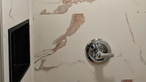 A bathroom with a shower, a sink, and a marble wall. - Star Inn & Suites (Chicago Heights)
