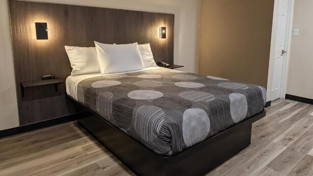 A modern hotel room with a large bed, a nightstand, and two wall-mounted lights. - Star Inn & Suites (Chicago Heights)