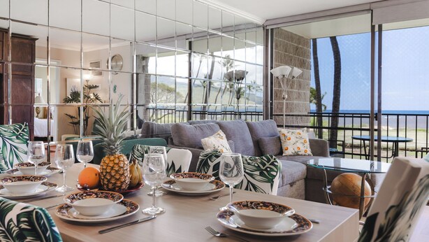 A dining area with a table set for four, tropical-themed decor, and a view of the ocean. - 🌅 Maui Magic! Panoramic Beachfront Stay! Ocean Views, Pool, Hot Tub, Sleeps 8🌊 (Kihei)