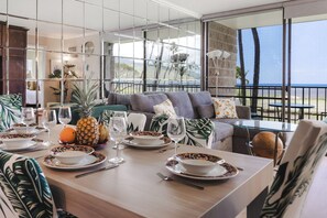 A dining area with a table set for four, tropical-themed decor, and a view of the ocean. - 🌅 Maui Magic! Panoramic Beachfront Stay! Ocean Views, Pool, Hot Tub, Sleeps 8🌊 (Kihei)