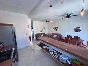 Une cuisine moderne dotée d’une cuisinière intégrée, d’un coin repas avec une longue table et des chaises en bois, et d’un ventilateur de plafond.