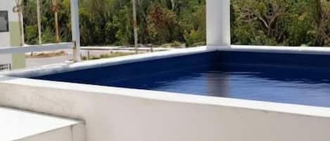 A pool with steps leading up to it, surrounded by a white structure and greenery in the background.