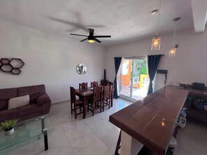 A modern living room with a dining area, a ceiling fan, and a view through a glass door. - Rooftop small pool | El Segundo (Puerto Morelos)