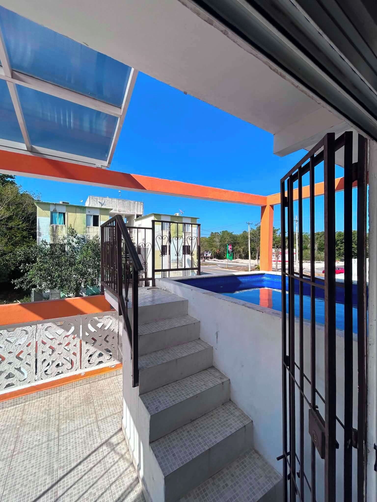 A pool area with a staircase leading to a covered deck, surrounded by a metal fence.