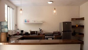 A modern kitchen with a central island, bar stools, a refrigerator, and a microwave. - Rooftop small pool | El Segundo (Puerto Morelos)